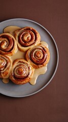 Fototapeta premium Delicious cinnamon swirl pastries with creamy icing on a minimalist grey plate