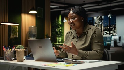 Black businesswoman greeting people on a video call network at office smiling, hosting a briefing meeting. Engaging in a virtual conversation, exchanging ideas about successful enterprise. Camera A. © DC Studio