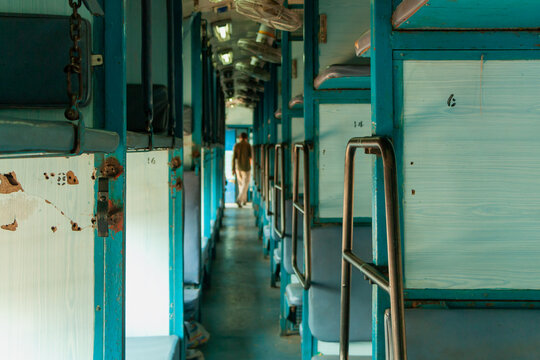 Perspective view inside an Indian sleeper class train featuring blue benches and ceiling fans