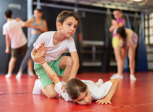 Teenage girl learns a hand grip in sparring with a boy during a workout. Children practice self-defense techniques in the gym