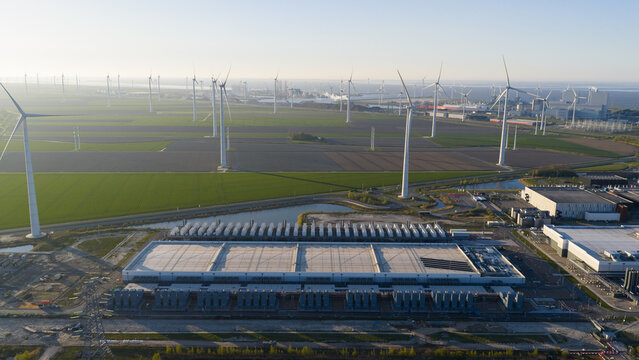 Aerial view of the Google GRQ data center complex surrounded by wind turbines and green fields under a clear sky in Eemshaven, Groningen, Netherlands.