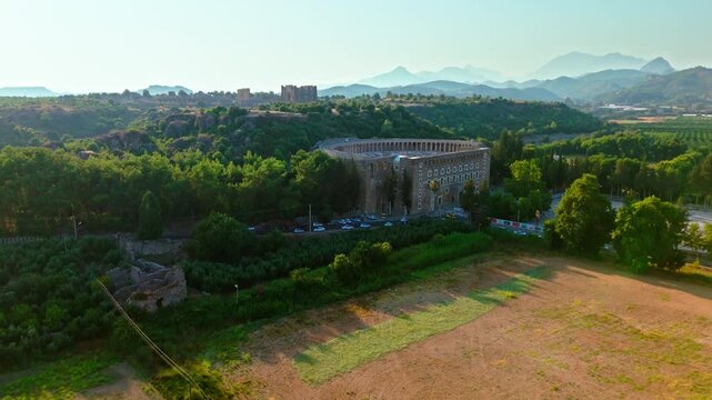 Drone aerial of Aspendos Theatre, Antalya, Turkey. Wide countryside view with the historic amphitheater and nearby fields.