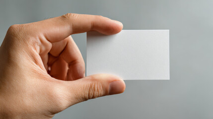 Fototapeta premium Hand holding a blank white rectangular card with a neutral gray background perfect for business or personal use with copy space for text or design ideas