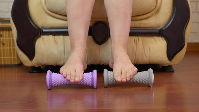 Woman massaging feet with spiky rollers for pain relief. Close up view of a woman's bare feet rolling on special spiky massagers for plantar fasciitis, providing deep tissue therapy, relaxation
