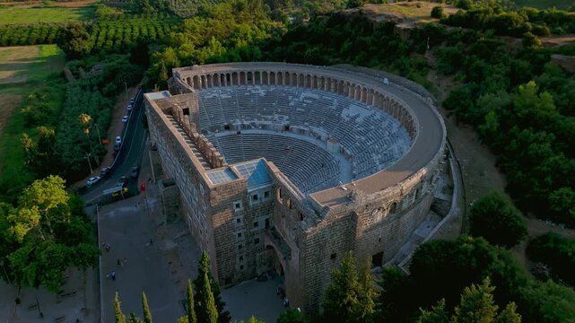 Aerial close view of Aspendos Theatre stage. Drone shot reveals ancient stone architecture and seating rows surrounded by greenery.
