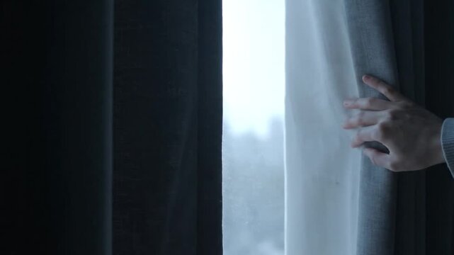 Hand peeking through a curtain.