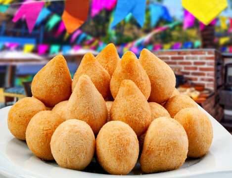 Brazilian chicken croquettes (coxinha) and fried appetizers on a plate with a colorful Festa Junina blurred background. Traditional Brazilian street food and party snacks