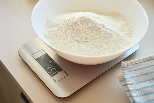 Bowl with flour sits on digital kitchen scale beside towel