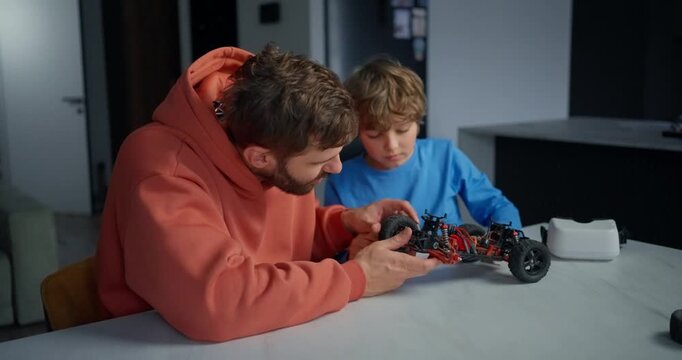 Father and young son repairing a small remote control car together at a kitchen table, concentrating on mechanical parts during a hands-on family project