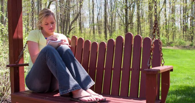 Female sitting on porch swing writing in notebook 4k