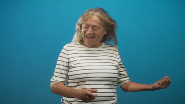 Senior woman with striped shirt, mouth open and hair whipping as she air guitars and headbanging in studio; joy.