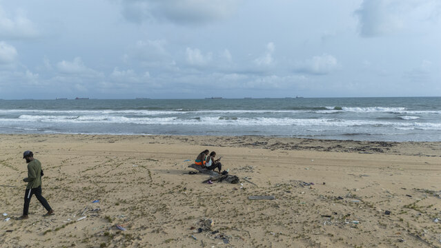 Aerial view of people relaxing on a sandy beach with gentle waves and cargo ships on the horizon in Badagry, Lagos, Nigeria.