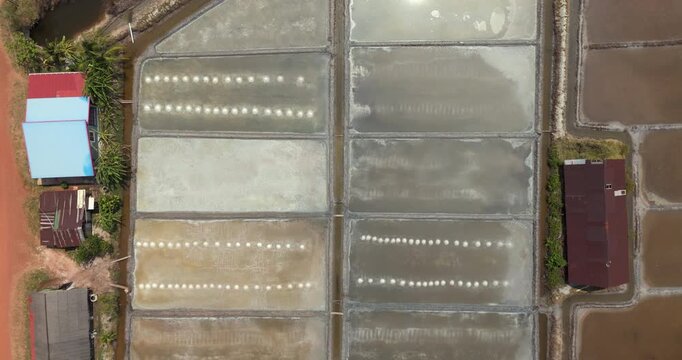 Aerial top down view of salt evaporation ponds with rows of salt mounds and nearby colorful buildings