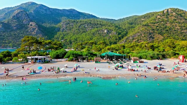 Drone view of Oludeniz Blue Lagoon, Turkey with umbrellas. People relax on the sandy beach by turquoise water and green mountains in summer.