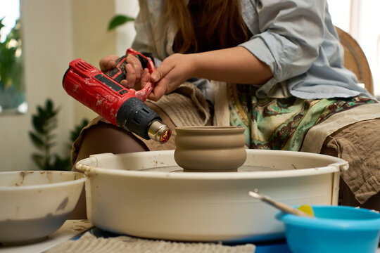 Portable heat gun being used by an artisan to stiffen wet clay on a spinning wheel.