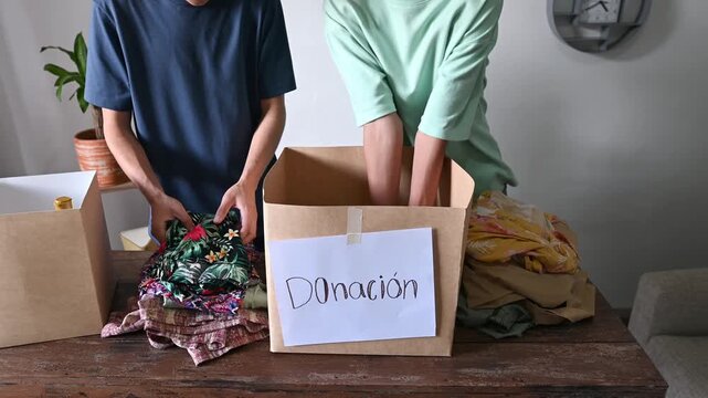 Close-up of young volunteers' hands putting clothes into boxes to donate them