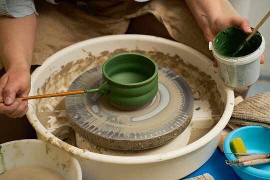 Artisan maker applying a decorative green underglaze to a rotating ceramic bowl.