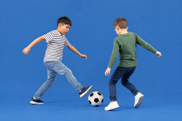 Fototapeta premium Two young boys playing soccer together in a studio with a blue background, childhood fun and physical activity for sports education and youth competition