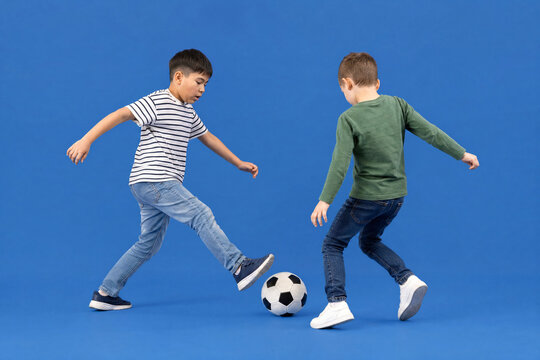 Two young boys playing soccer together in a studio with a blue background, childhood fun and physical activity for sports education and youth competition