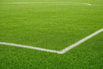Obraz premium Green artificial turf of a soccer field with white boundary lines in bright daylight, sports background for competition and athletic training on a professional stadium pitch