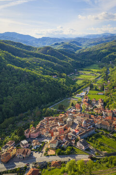 Aerial view of the historic Borgo Rotondo in Varese Ligure, featuring colorful houses and ancient stone towers surrounded by lush green hills and forested valleys Varese Ligure, Liguria, Italy.