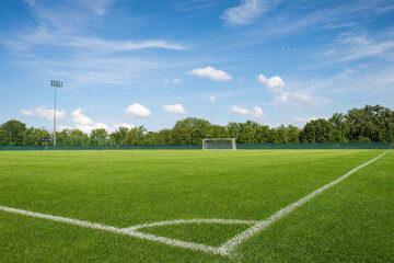 Naklejka premium Empty soccer field with green grass and white corner line under a blue sky, professional sports pitch with goal post and stadium lights for competition and training