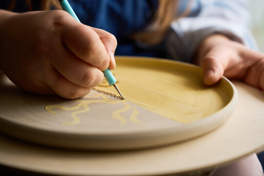 Detailed view of a sharp sgraffito tool etching designs onto raw clay surface.