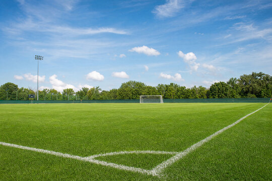 Empty soccer field with green grass and white corner line under a blue sky, professional sports pitch with goal post and stadium lights for competition and training