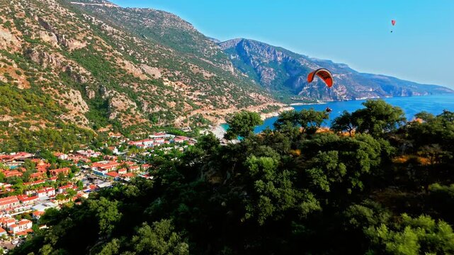 Aerial view of paraglider over Oludeniz Blue Lagoon, Turkey mountains. Green forest, rocky peaks and sunny sky create a scenic adventure travel scene.