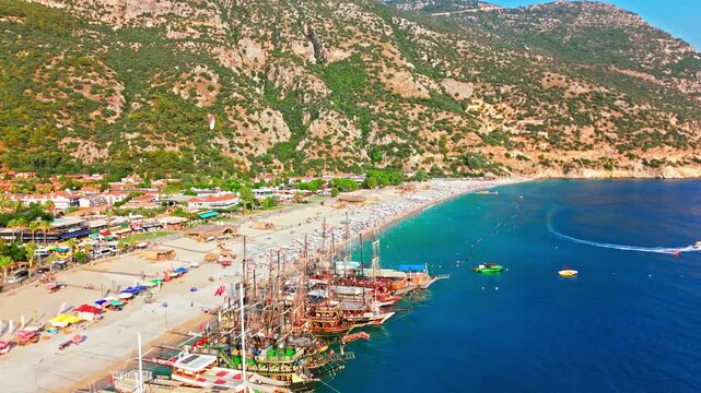 Aerial view of Oludeniz Blue Lagoon, Turkey beach. People relax under umbrellas by turquoise water with boats and green mountains.