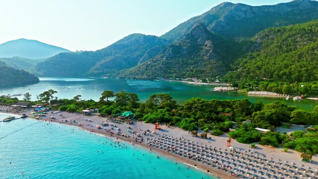 Aerial view of Oludeniz Blue Lagoon, Turkey beach. People relax under umbrellas by turquoise water and green mountains.