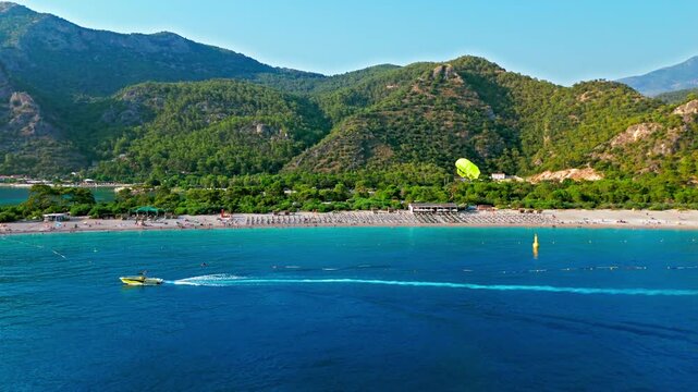 Drone view of Oludeniz Blue Lagoon, Turkey coastline. Blue sea, forested mountains and sunny shore create a scenic Mediterranean view. Tourists paragliding in Turkey.