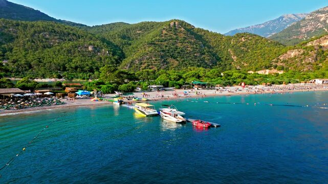 Drone view of Oludeniz Blue Lagoon, Turkey beach and boats. People relax by the shore as boats float on turquoise water near green mountains.
