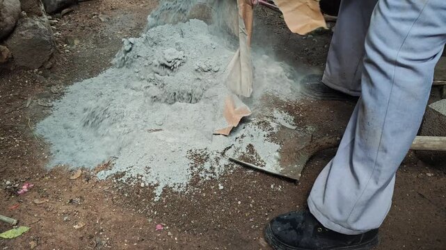 Pouring a small bag of cement onto a sand pile