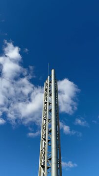 Steel heating pipe tower against sky narrow stainless column rises into vivid blue with drifting white clouds, visible lattice