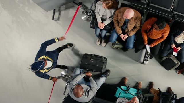 Top down shot of gate agent giving flight announcement in airport, removing stanchion for tourists. Airline worker inviting people to queue up for boarding gate, doing crowd control