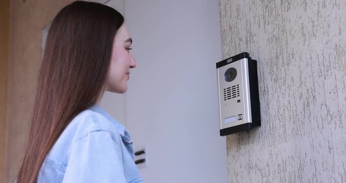 Woman pressing button on intercom panel outdoors
