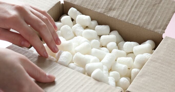 Woman putting styrofoam pieces into cardboard box at pink table, closeup