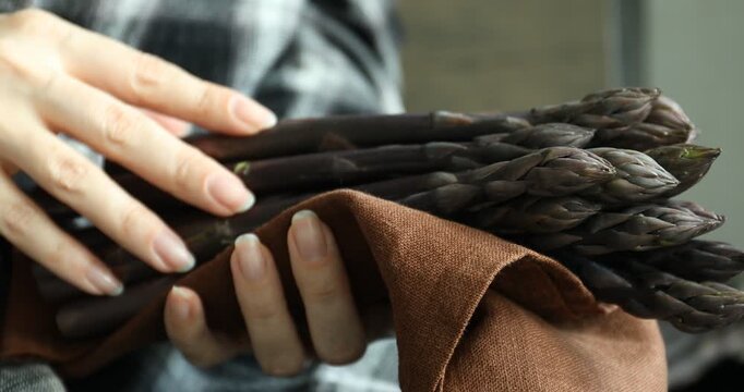 Woman holding raw purple asparagus spears on blurred background, closeup