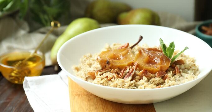 Tasty oatmeal porridge with caramelized pear, nuts, mint, honey and fresh fruits on wooden table, closeup