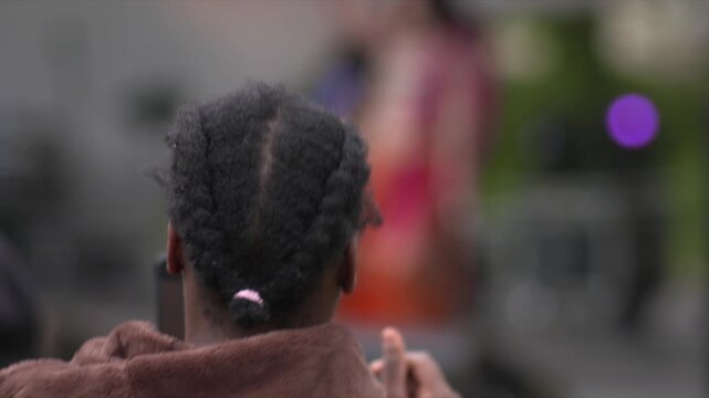 Woman dances in time to music cell phone video rear view hair braids