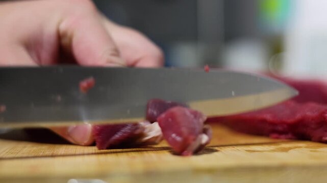 Horizontal 4K video close up. Chef cutting piece of raw fresh juicy beef meat with knife on wooden cutting board on kitchen table in no vegan cafe. Male hand. Man preparing dinner, healthy food, lunch