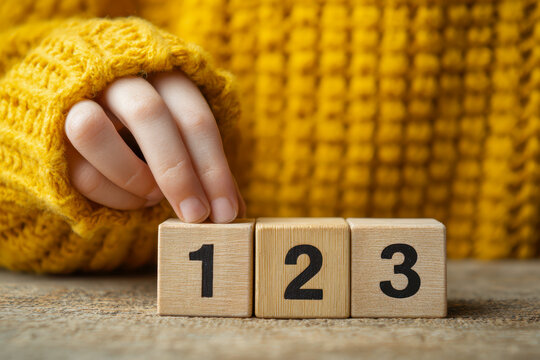 Child's hand in cozy mustard sweater arranging wooden blocks numbered one, two, and three on rustic table for early learning concept