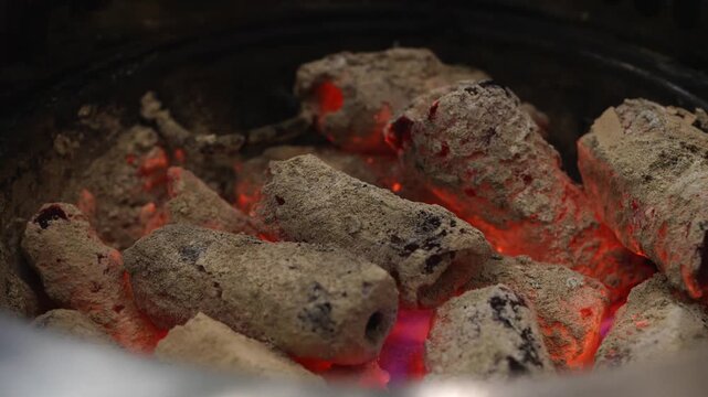Glowing hot charcoal briquettes with white ash in a round barbecue grill. Close-up view showing red embers and intense heat. Perfect for outdoor cooking, BBQ parties, and grilling themes.