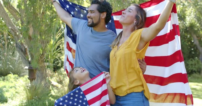 Diverse family seeing child with small flag, man wrapping arm, lifting large flag on sunlit lawn