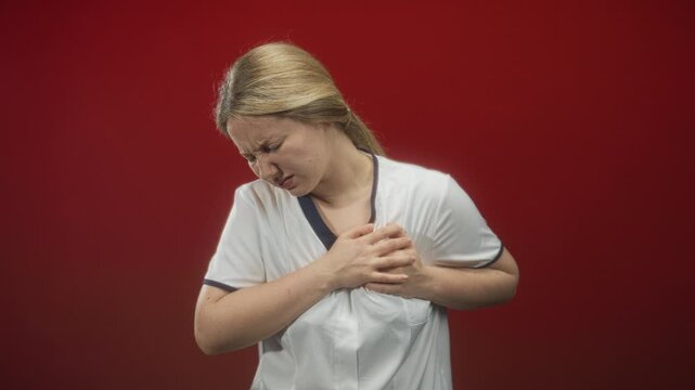 Woman nurse in white uniform clutching chest, grimacing and pressing sternum as if heartattack in studio; pain emergency.