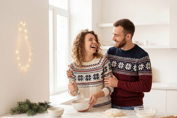 Fototapeta premium Cheerful young couple playfully cooking holiday treats in modern kitchen