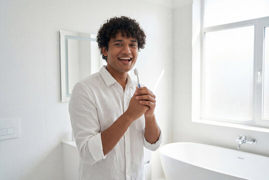 Cheerful young man sings into toothbrush pretending it is a microphone in a white bathroom