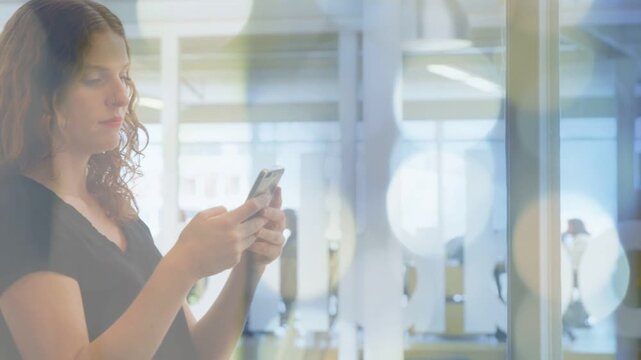 Woman standing by glass door holding phone, animated notification popping, checking work messages
