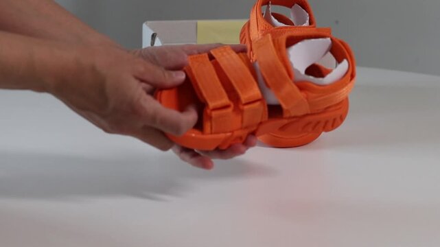 Woman examines sandals, unfastens and fastens hook-and-loop. Check children's sandals, choose shoes for the child. Check out the bright orange velcro sandals with an open heel